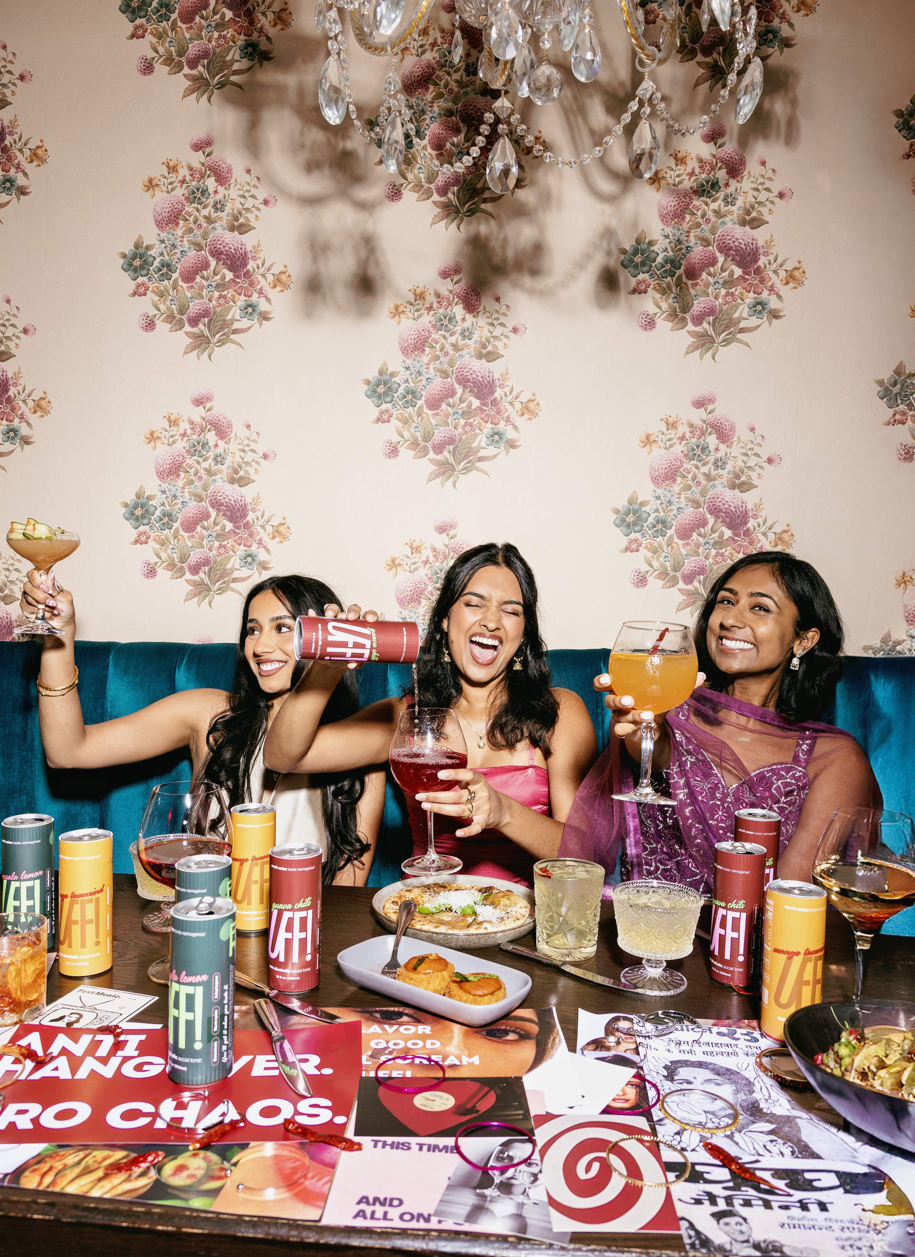 Three friends toasting UFF! spritzes under a chandelier
